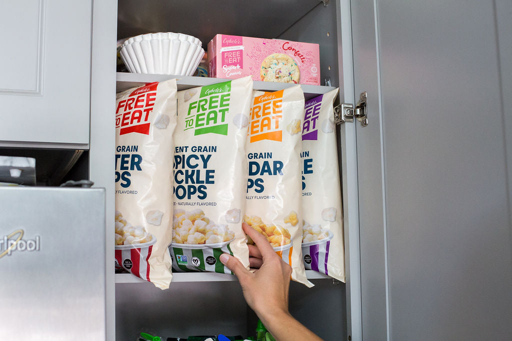 woman reaching into cupboard with a box of Confetti Soft Baked Cookie box and 4 bags of Ancient Grain pops