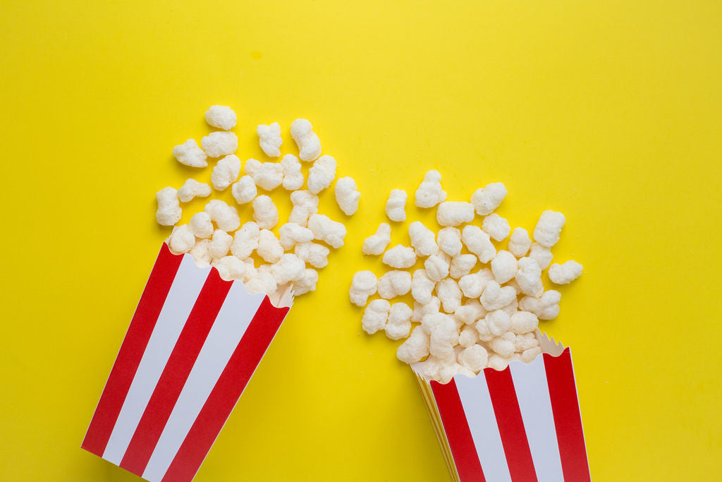 Ancient Grain Pops in red and white popcorn containers spilling out on yellow background