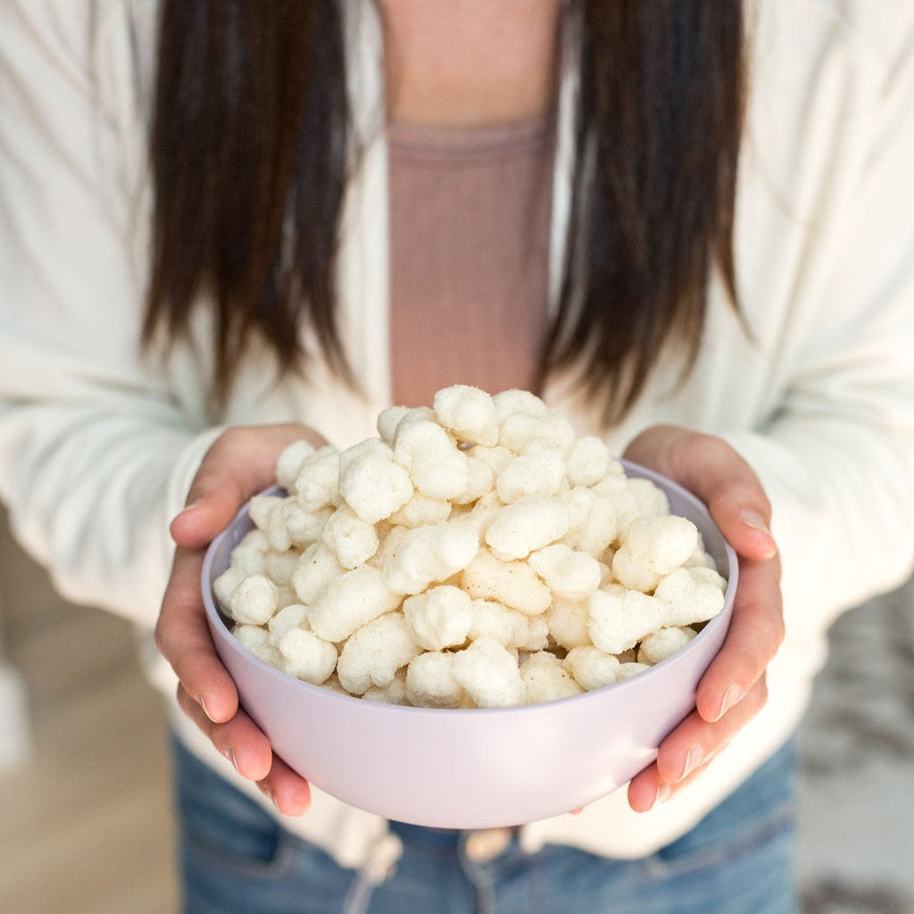 Woman with White jacket and jeans holding a white bowl of Kettle Ancient Grain Pops