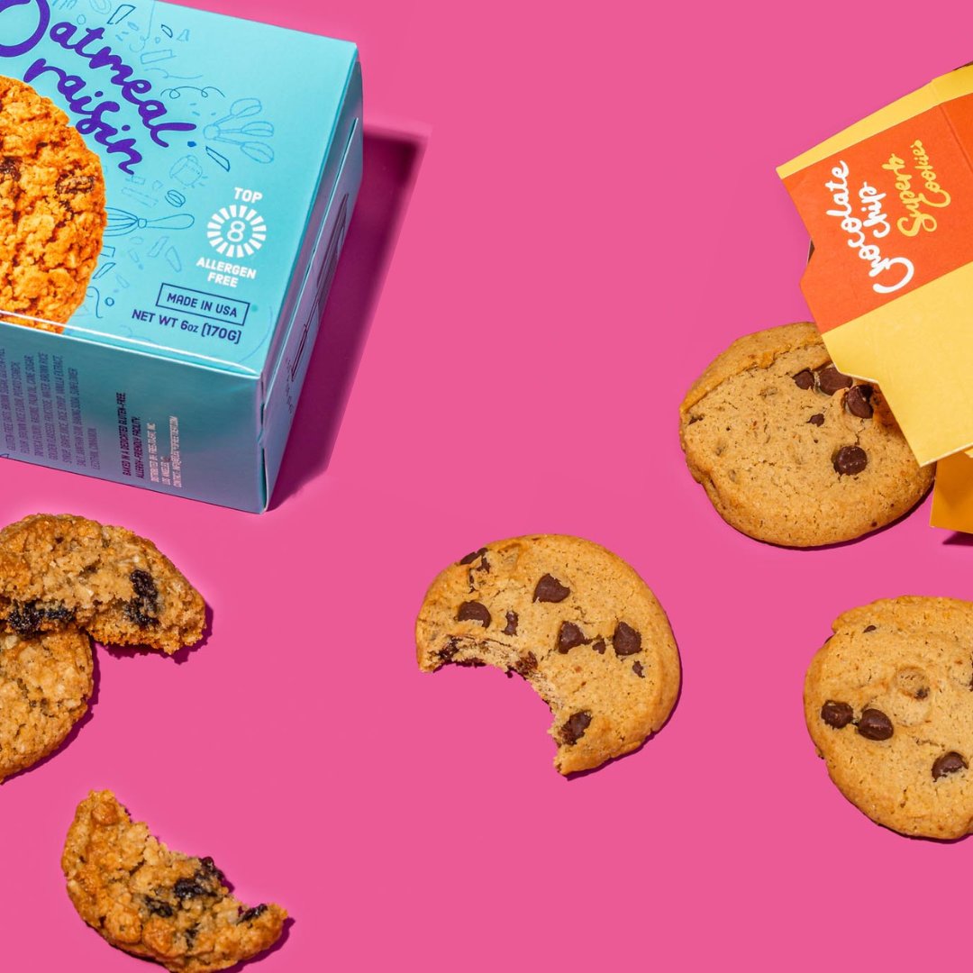 Oatmeal Raisin Box and Chocolate Chip Cookies box with cookies spilling out on pink background. All Cookies Headline at bottom