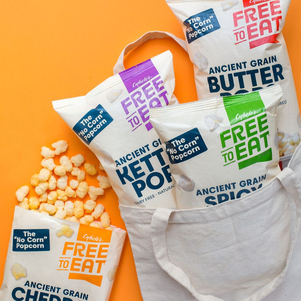 3 backs of Ancient Grain Pops in natural colored tote with one bag on orange background spilling out